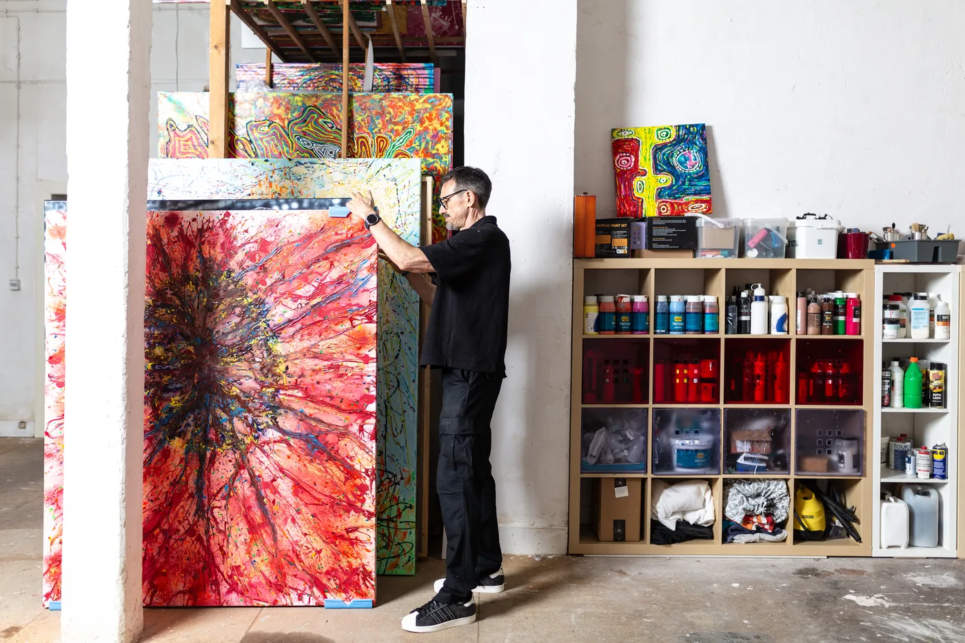 The artist sorting large-format canvases in the studio in front of the materials shelf